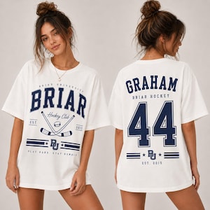 May include: A white short-sleeve t-shirt featuring navy blue graphics. The front displays 'BRIAR UNIVERSITY HOCKEY CLUB' with crossed hockey sticks and a puck. The back features the name 'GRAHAM' above the large number '44' and 'BRIAR HOCKEY'.