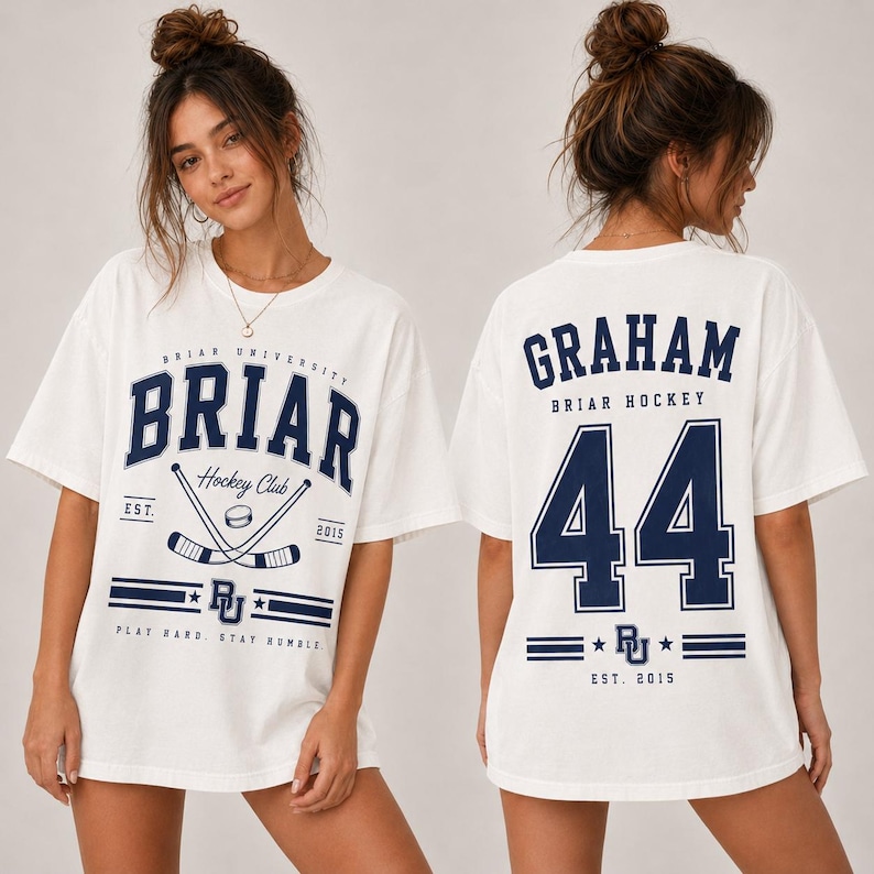 May include: A white short-sleeve t-shirt featuring navy blue graphics. The front displays 'BRIAR UNIVERSITY HOCKEY CLUB' with crossed hockey sticks and a puck. The back features the name 'GRAHAM' above the large number '44' and 'BRIAR HOCKEY'.