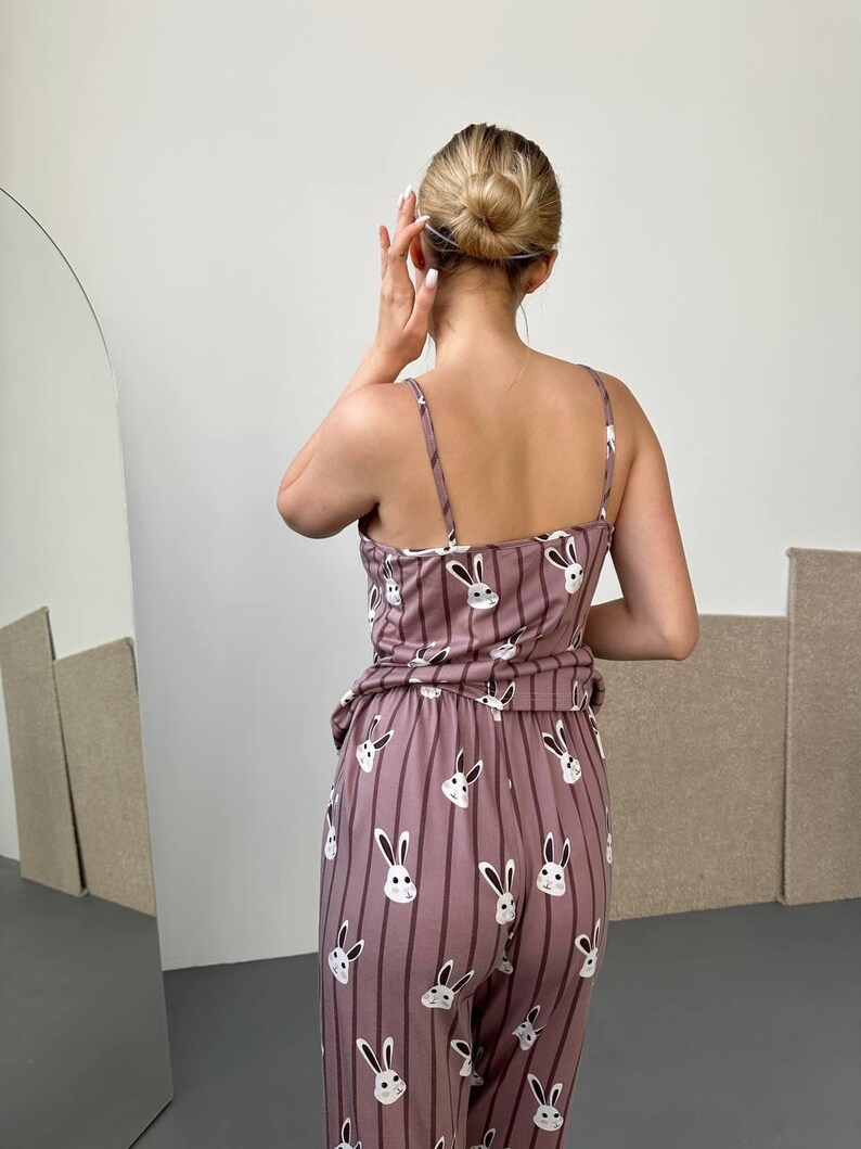 K&ouml;nnte beinhalten: Mauvefarbenes Pyjama-Set mit Hasenmuster. Das Set besteht aus einem Camisole-Top und einer passenden Hose mit vertikalen Streifen. Die Hasengesichter sind wei&szlig; mit schwarzen Augen und Schnurrhaaren. Das Model ist von hinten zu sehen.