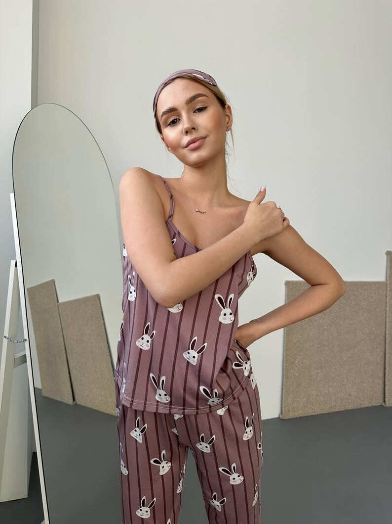 K&ouml;nnte beinhalten: Mauvefarbenes Pyjama-Set mit Hasenmuster. Das Set beinhaltet ein Camisole-Top, eine Hose und ein Stirnband. Der Pyjama hat vertikale Streifen und ein sich wiederholendes Muster aus wei&szlig;en Hasengesichtern.