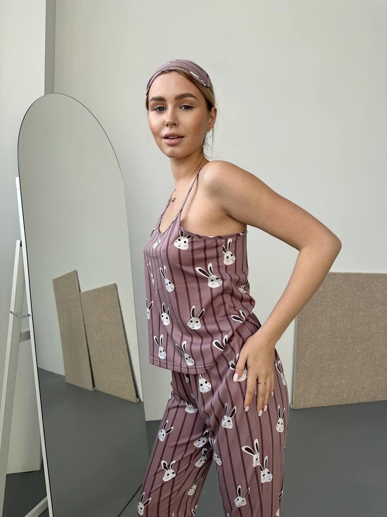 K&ouml;nnte beinhalten: Mauvefarbenes Pyjama-Set mit Hasenmuster. Das Set beinhaltet ein Tanktop, eine Hose und ein passendes Stirnband. Der Pyjama hat vertikale Streifen und wei&szlig;e Hasengesichter. Das Tanktop hat d&uuml;nne Tr&auml;ger.