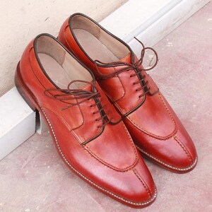 May include: A pair of red leather dress shoes with brown laces. The shoes have a classic design with a rounded toe and a stitched sole. The shoes are approximately 11 inches long.