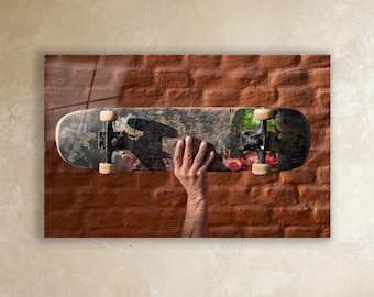 May include: A well-worn skateboard with black trucks and beige wheels is held up against a red brick wall. The deck shows signs of use with various stickers and wear marks. The skateboard is a classic piece of skateboarding equipment.