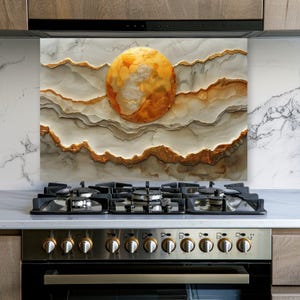 May include: A rectangular kitchen backsplash panel featuring a marbled design in shades of white, gray, and beige. A large, circular, textured golden-orange sun sits in the center, surrounded by layered, wavy horizontal lines with gold accents.