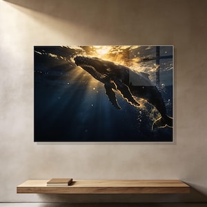 May include: A rectangular wall art print featuring a humpback whale swimming through deep blue ocean water. Golden sunlight filters from the surface, illuminating the whale's silhouette and creating bright highlights along its body and fins.