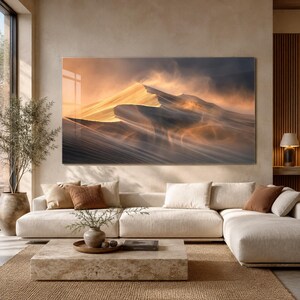 Op de afbeelding: Een grote rechthoekige wandkunstprint met een landschap van gouden zandduinen onder een dramatische, donkere lucht. De scène vangt het contrast tussen de heldere, zonovergoten ruggen van de duinen en de diepe, schaduwrijke valleien in goud- en grijstinten.
