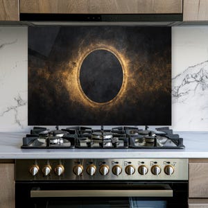 May include: A rectangular kitchen splashback panel featuring a dark, textured black background with a prominent, glowing golden oval ring centered in the middle, creating a high-contrast visual effect behind a stainless steel gas stove.