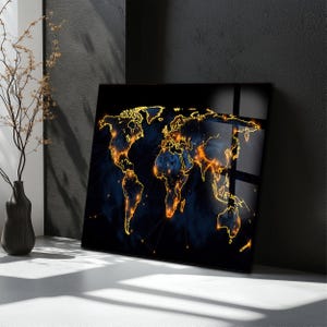 May include: A square, black world map art print with gold outlines of continents and glowing orange city lights. The background features a dark blue, smoky effect. The artwork is leaning against a dark gray wall.