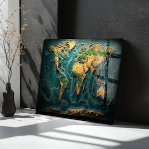 Puede incluir: Una obra de arte cuadrada con un mapa del mundo texturizado y un acabado brillante. Los continentes están representados en tonos dorados, verdes y marrones, sobre un océano verde azulado profundo. La obra está apoyada contra una pared gris oscura.