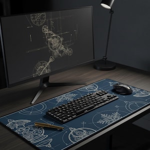 May include: A computer desk setup featuring a blue and white patterned desk mat with a keyboard, mouse, and pen. A black monitor displays a gold-colored blueprint design. A black desk lamp is also visible.