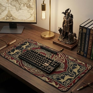 Puede incluir: Un teclado mecánico negro descansa sobre una alfombrilla de escritorio decorativa con un diseño celta rojo, negro y dorado. Una estatua vikinga de bronce y libros sobre mitología nórdica también están sobre el escritorio de madera.