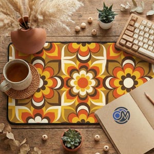 May include: A rectangular mouse pad with a retro floral pattern in shades of orange, yellow, brown, and white. The pad is surrounded by a black border. A cup of tea, a keyboard, and a notebook are on the wooden surface.