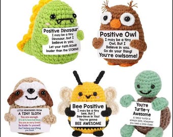 May include: Five crocheted stuffed animals: a green dinosaur, a brown owl, a sloth, a yellow bee, and a green turtle. Each animal holds a sign with an inspirational message. The dinosaur says "Positive Dinosaur". The owl says "Positive Owl". The sloth says "Little Reminders From A Tiny Sloth". The bee says "Bee Positive". The turtle says "You're Turtle-y Awesome".