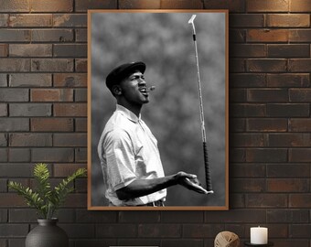 May include: Monochrome framed print of a person in golf attire, holding a golf club and smoking a cigar. The person is wearing a cap and a collared shirt. The background is a blurred golf course.