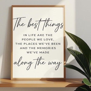 Op de afbeelding: Een ingelijste print met de tekst "The best things in life are the people we love, the places we've been and the memories we've made along the way." De lijst is lichtbruin, de achtergrond is gebroken wit.