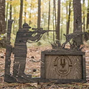 Könnte beinhalten: Ein dunkelbrauner Holzausschnitt mit der Silhouette eines Jägers, der mit einem Gewehr auf einen springenden Hirsch zielt. Der Sockel enthält einen rechteckigen Rahmen mit dem eingravierten Text Laser Impressions und einem Laserschneid-Symbol.