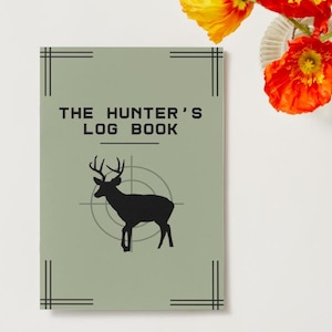 May include: A sage green log book with the text "THE HUNTER'S LOG BOOK" in black. A black silhouette of a deer with antlers is centered on the cover, superimposed over a target. Black lines frame the edges of the book. Orange and yellow flowers are in the background.