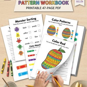 Puede incluir: Un cuaderno de patrones de jardín de infancia imprimible de 47 páginas. El cuaderno incluye actividades de combinación de colores, clasificación de monstruos y patrones de colores. La imagen muestra crayones, lápices y una mano usando un lápiz amarillo.