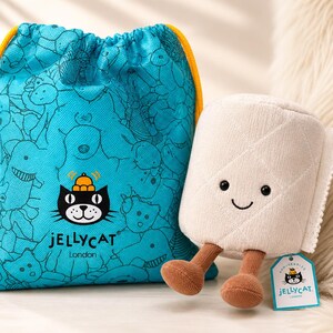 May include: A plush toy roll of toilet paper with a smiling face and brown legs, next to a blue drawstring bag with a pattern of cartoon animals. The bag has a yellow drawstring and the Jellycat London logo.