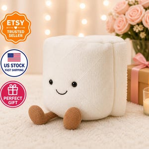 May include: A white plush toy shaped like a roll of toilet paper with a smiling face and brown feet. The toy has black eyes and a stitched smile. The image also includes a bouquet of pink roses and a gift box.