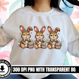 May include: White sweatshirt with a design of three cartoon bunnies with leopard print fur, floral details, and bow ties, each holding a basket of Easter eggs. The image includes the text "300 DPI PNG WITH TRANSPARENT BG" and "DIGITAL FILE NO PHYSICAL PRODUCT".