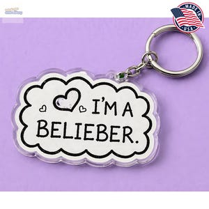 May include: A clear acrylic keychain with a white cloud-shaped design and the text "I'M A BELIEBER." The keychain features a silver keyring and a small green accent. A "Made in USA" sticker with an American flag is visible.