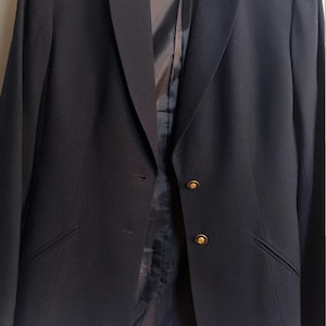 May include: A dark navy blue blazer featuring a notched lapel, long sleeves, and two gold-toned metal buttons on the front closure. The interior is lined with a matching dark navy fabric, and the inner label reads KASPER A.S.L. size 10.
