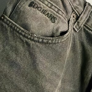 May include: Close-up of a pair of faded olive green jeans. The jeans feature a classic five-pocket design with the brand name "BDG JEANS" embroidered on the back pocket. The fabric has a textured appearance.