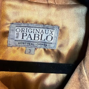May include: A tan suede jacket with a smooth gold-toned satin lining. A rectangular grey fabric label is stitched to the interior, featuring the text PARO ORIGINAUX PABLO MONTREAL CANADA and a small tag below with the number 3.