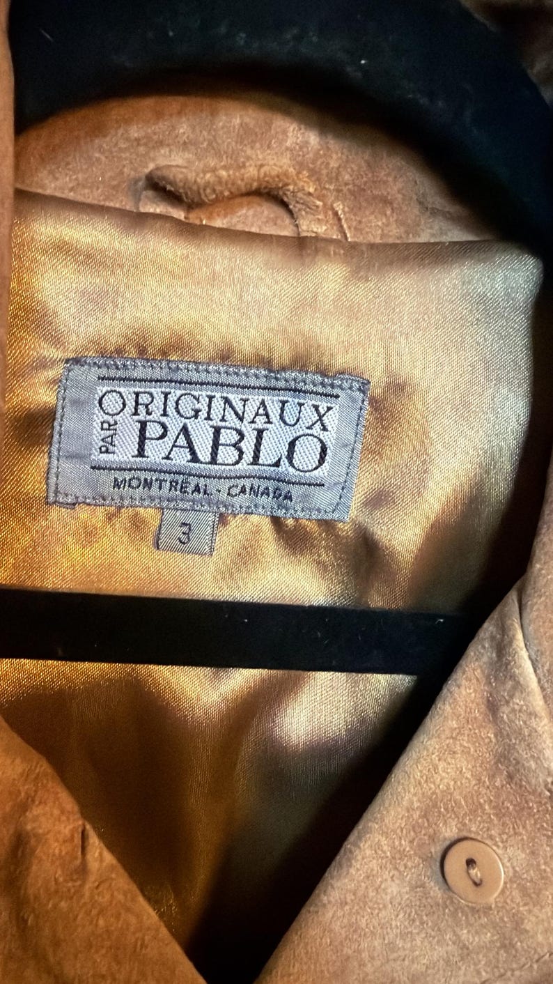 May include: A tan suede jacket with a smooth gold-toned satin lining. A rectangular grey fabric label is stitched to the interior, featuring the text PARO ORIGINAUX PABLO MONTREAL CANADA and a small tag below with the number 3.