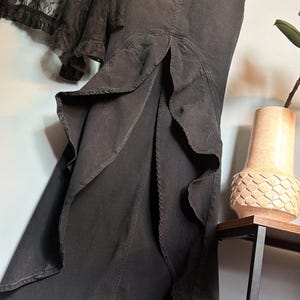 May include: A black denim skirt with a ruffled hem and a matching black lace top. The skirt has a high waist and a split front. The lace top is sheer and has a floral pattern. The clothing is hanging on a hanger.