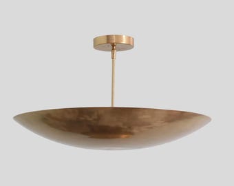 May include: A brass-colored, bowl-shaped pendant light fixture. The light has a wide, shallow bowl and a central rod connected to a circular ceiling mount. The fixture is suspended from the ceiling.