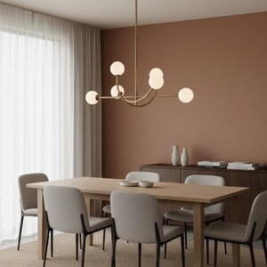 Pu&ograve; includere: Una sala da pranzo moderna con un tavolo in legno chiaro e sei sedie grigie imbottite. Sopra il tavolo &egrave; appeso un lampadario dorato con luci sferiche. La stanza ha una palette di colori neutri con una parete marrone e un tappeto beige.