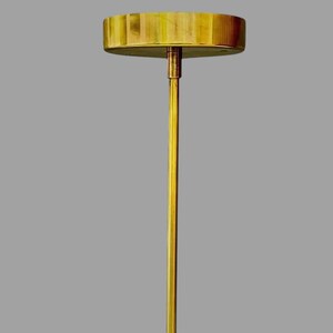 May include: A gold-colored, minimalist table lamp with a round, wooden top and a slender, vertical stem. The lamp's design is simple and elegant, suitable for various interior styles. The lamp's height is approximately 24 inches.