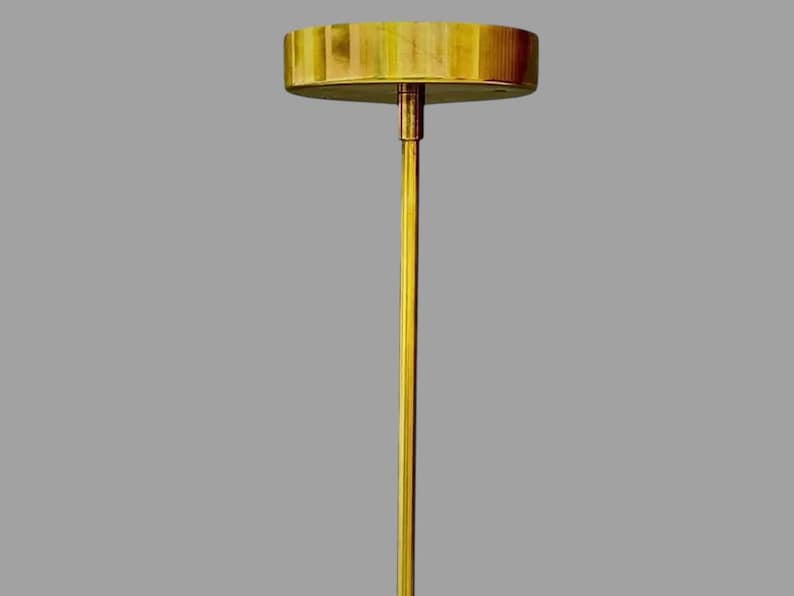 May include: A gold-colored, minimalist table lamp with a round, wooden top and a slender, vertical stem. The lamp's design is simple and elegant, suitable for various interior styles. The lamp's height is approximately 24 inches.