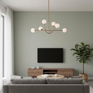 Pu&ograve; includere: Un moderno soggiorno con un divano grigio, un mobile TV in legno e un tavolino rotondo. Un grande televisore nero &egrave; montato a parete. Un lampadario in ottone con luci a globo bianche pende dal soffitto. Una pianta in vaso aggiunge verde.