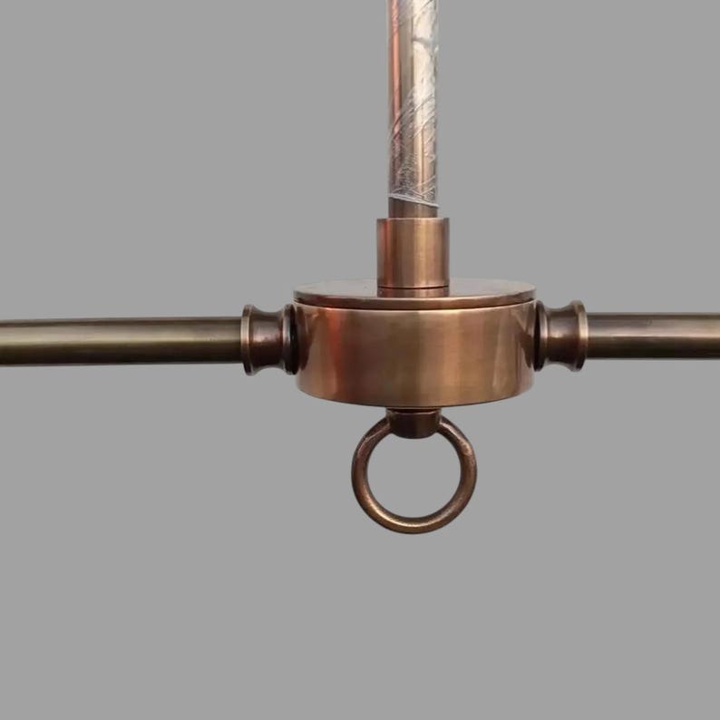 May include: Close-up of a bronze-colored ceiling light fixture. The fixture has a central circular housing with a ring at the bottom and three horizontal arms extending outwards. A vertical rod extends upwards from the center.