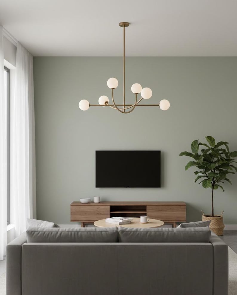 Pu&ograve; includere: Un moderno soggiorno con un divano grigio, un mobile TV in legno e un tavolino rotondo. Un lampadario dorato con luci sferiche &egrave; appeso al soffitto. Un grande televisore a schermo piatto nero &egrave; montato a parete e una pianta in vaso aggiunge verde.