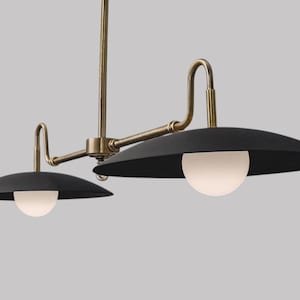 May include: A contemporary two-light pendant light. It has two black, saucer-shaped shades, each with a white globe light. The arms and central support are brass-coloured.