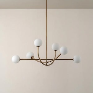 Pu&ograve; includere: Un lampadario moderno con finitura in ottone e sei paralumi sferici in vetro bianco. L'apparecchio &egrave; sospeso al soffitto da un'unica asta. Il design &egrave; minimalista ed elegante, adatto a vari stili di interni.