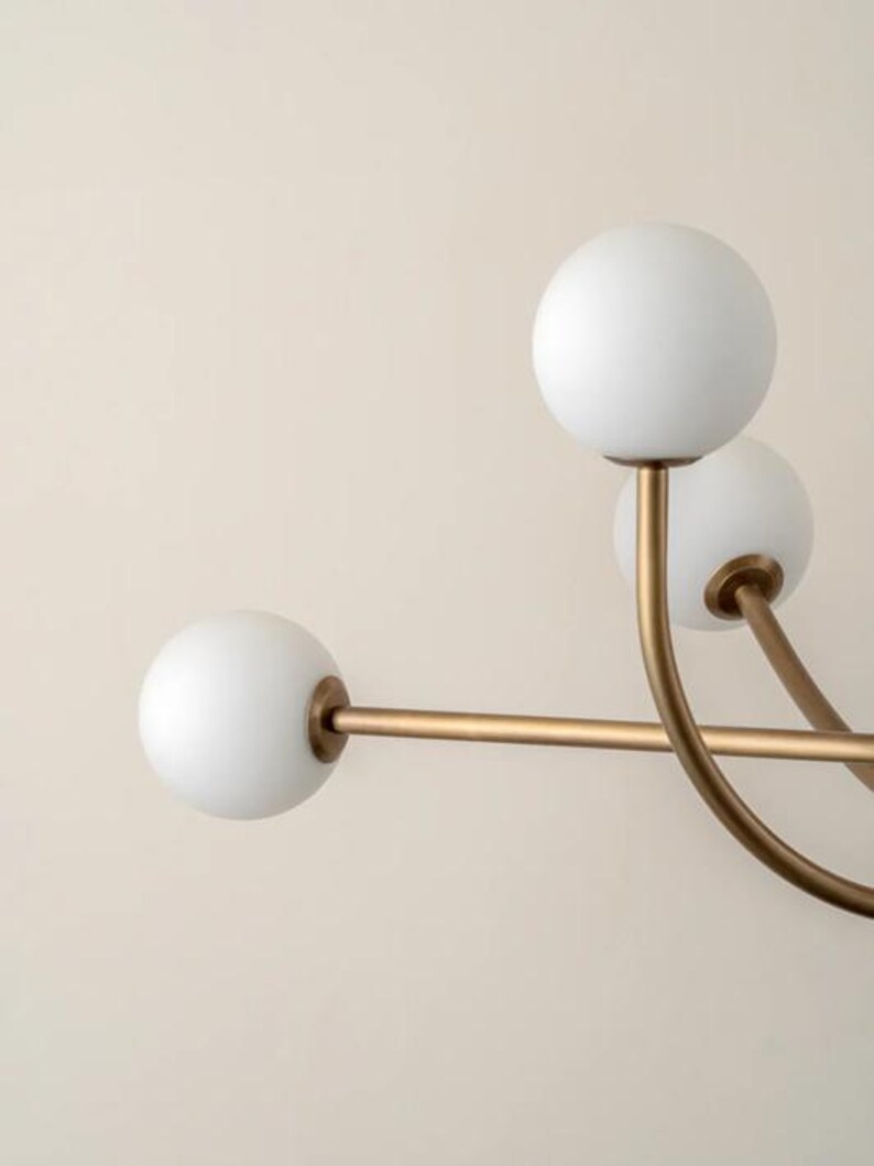 Pu&ograve; includere: Un lampadario moderno con una struttura dorata e bracci curvi. Ogni braccio sostiene un globo di vetro bianco e sferico. L'apparecchio &egrave; progettato con un'estetica minimalista, adatta a vari stili di interni.