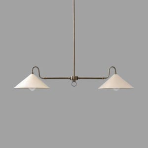 May include: A two-light pendant light fixture with a bronze finish. The fixture has two off-white cone-shaped shades and a central ring detail. The light bulbs are visible within the shades. The fixture is suspended from a single rod.