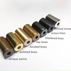 Pu&ograve; includere: Una collezione di campioni di ferramenta cilindrica in metallo con varie finiture, tra cui patina antica, ottone lucido, ottone spazzolato, ottone grezzo, ottone brunito, nero antico e cromo lucido. Ogni pezzo ha un foro centrale. Etichette di testo identificano ogni finitura.