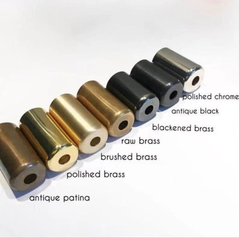 Pu&ograve; includere: Una collezione di campioni di ferramenta cilindrica in metallo con varie finiture, tra cui patina antica, ottone lucido, ottone spazzolato, ottone grezzo, ottone brunito, nero antico e cromo lucido. Ogni pezzo ha un foro centrale. Etichette di testo identificano ogni finitura.