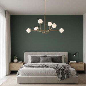 Pu&ograve; includere: Una camera da letto moderna con un letto con lenzuola e cuscini grigi, comodini in legno e un lampadario dorato con luci sferiche. La parete &egrave; dipinta di verde scuro e la stanza ha un design minimalista.