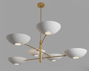 May include: A modern chandelier with six white, bowl-shaped shades. The shades are suspended from a central gold-colored stem and arms. Each shade has a light source, creating a warm glow. The fixture is designed for indoor use.