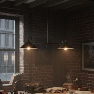 May include: A black, industrial-style pendant light fixture with two cone-shaped shades illuminates a vintage office space. The fixture hangs above a wooden desk with a typewriter, papers, and a framed picture against a brick wall. The room is lit by natural light from a large window.