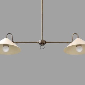 May include: A two-light pendant light fixture with a vintage aesthetic. The fixture has a central rod with a horizontal bar extending to each side. Each side holds a cream-colored, cone-shaped shade with a lightbulb.