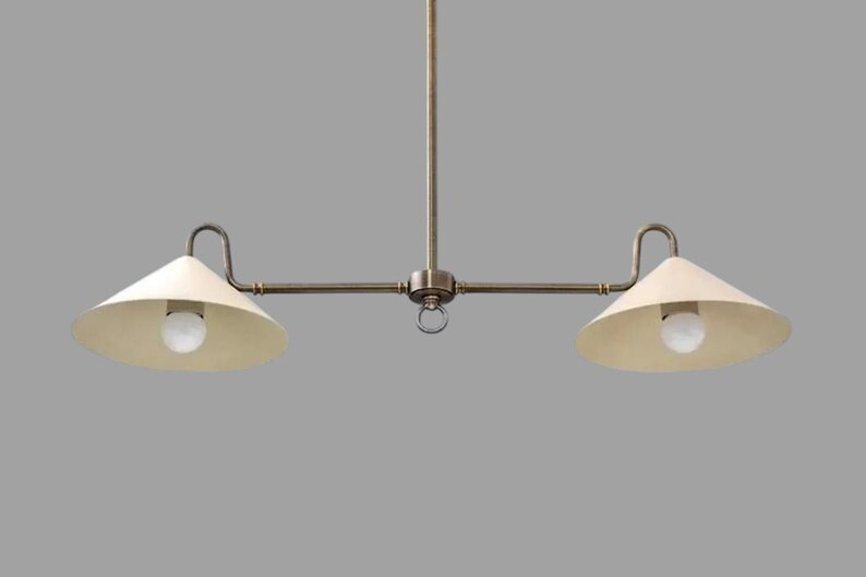 May include: A two-light pendant light fixture with a vintage aesthetic. The fixture has a central rod with a horizontal bar extending to each side. Each side holds a cream-colored, cone-shaped shade with a lightbulb.