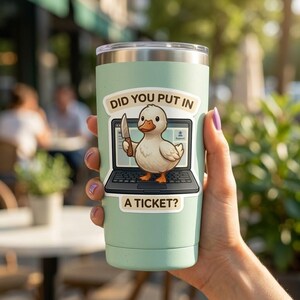 Puede incluir: Un vaso térmico verde claro con tapa plateada. Una pegatina en el vaso muestra un pato de dibujos animados sosteniendo un cuchillo frente a una pantalla de portátil. El texto de la pegatina dice "DID YOU PUT IN A TICKET?"